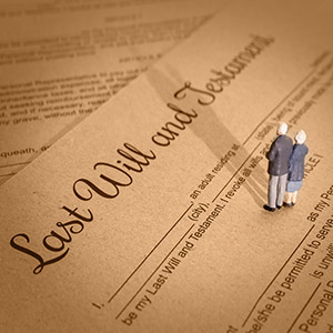 Overhead shot of a Last Will and Testament document with two miniature figures of an elderly couple standing on it, symbolizing estate planning
